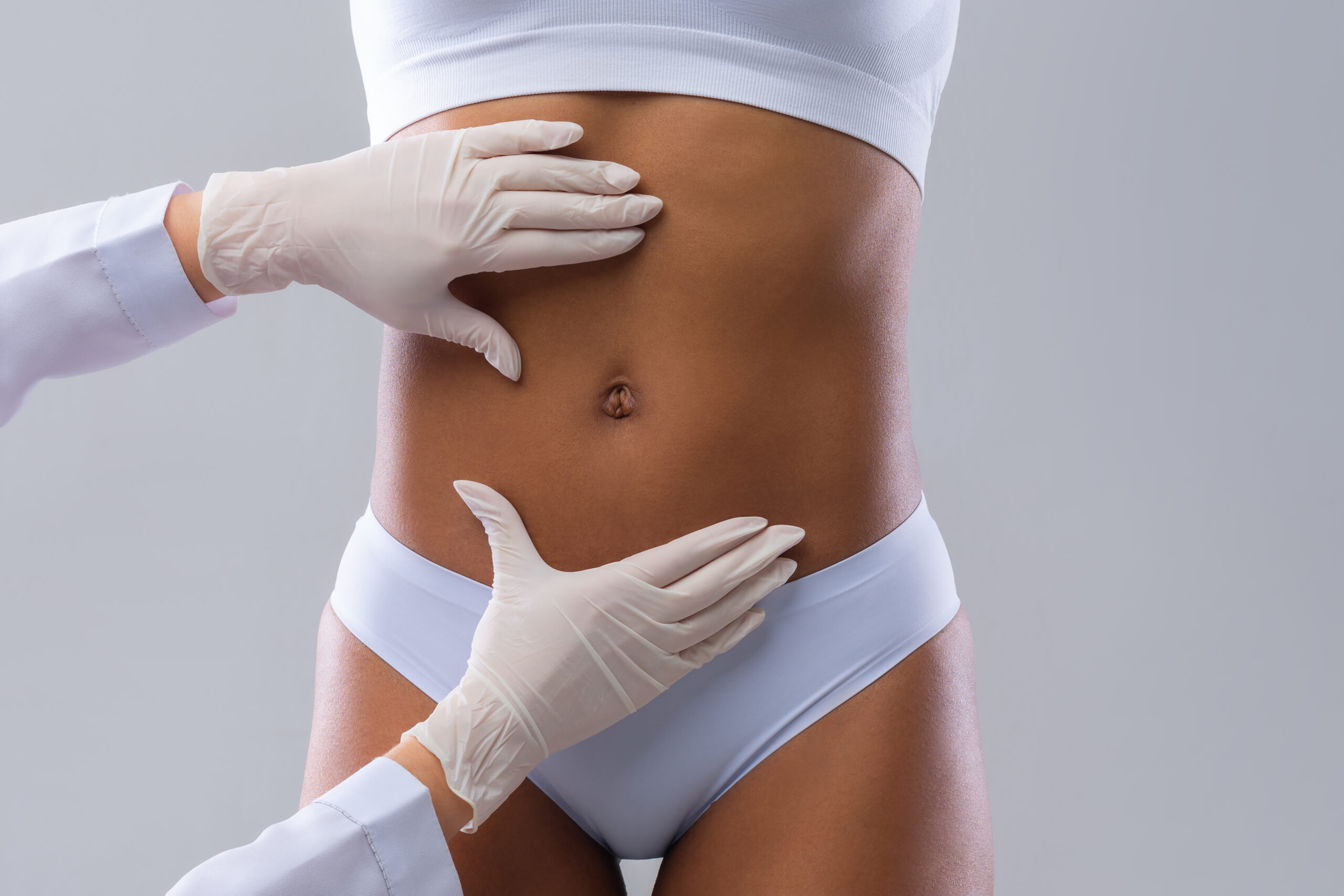 Cropped of plastic surgeon hands checking afro woman belly before beauty procedure, liposuction concept